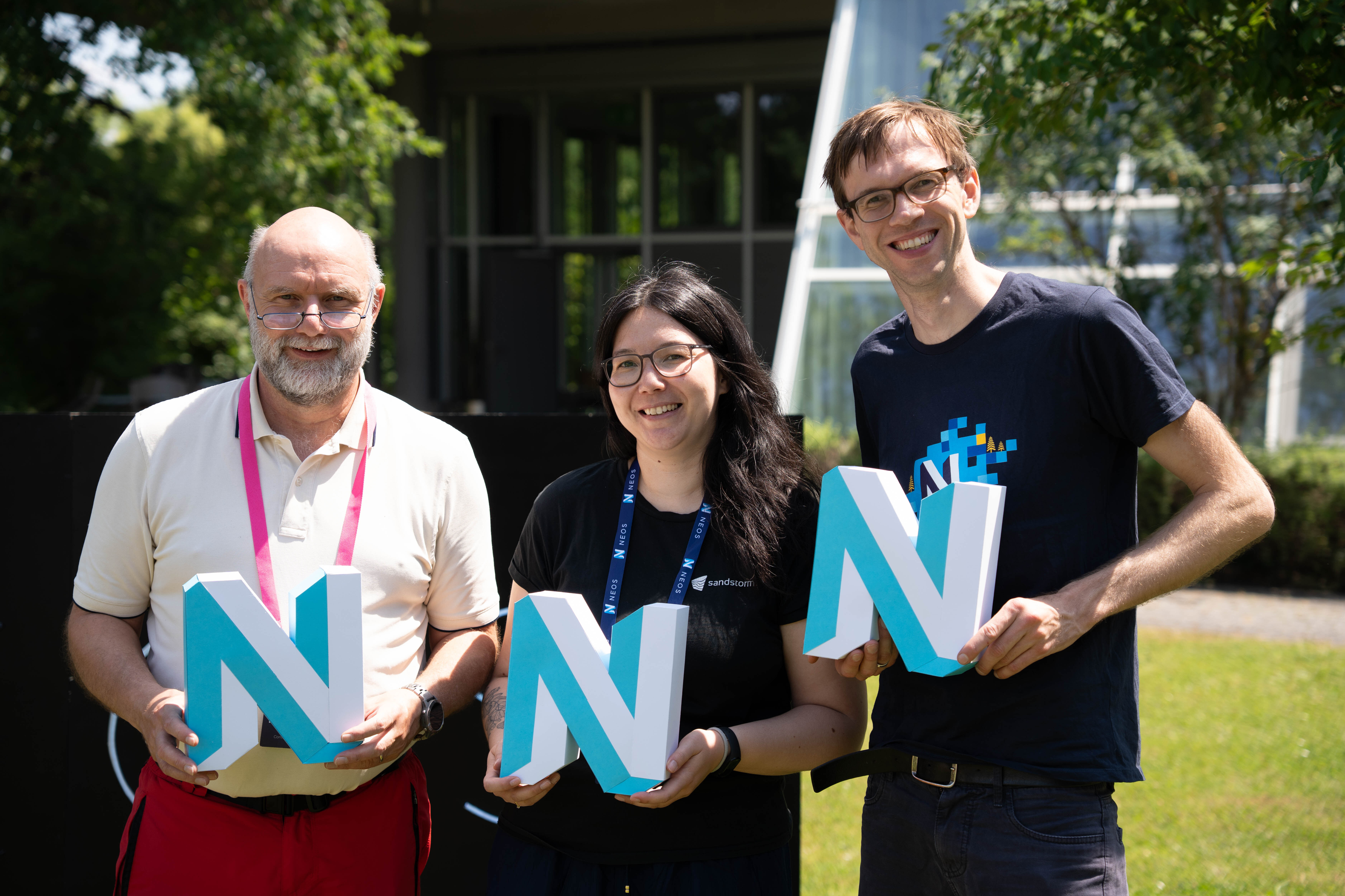 Jürgen, Sebastian and Marika holding a Neos Paper Logo at Neos Con 2025